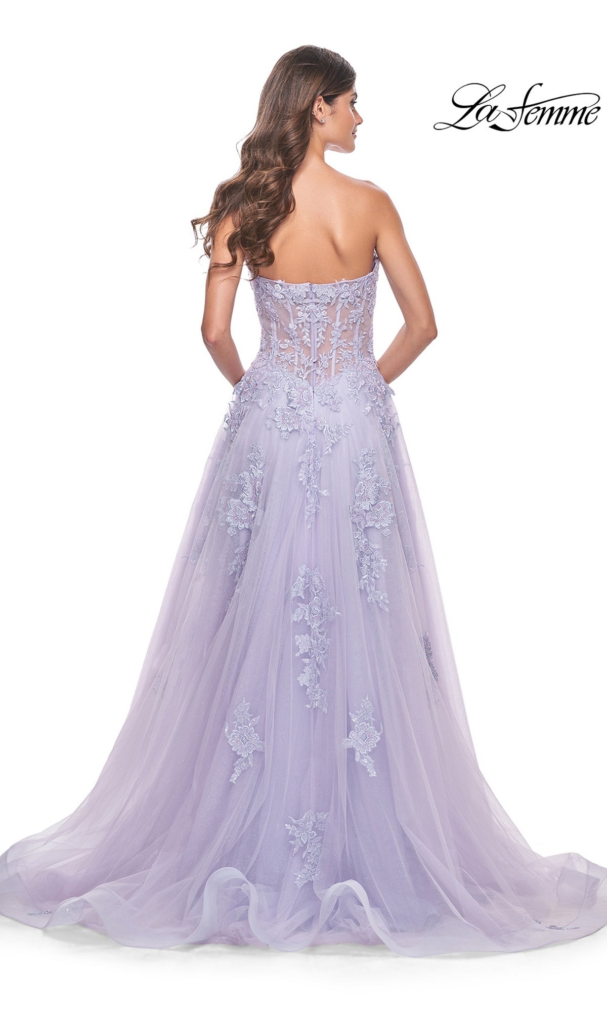 Wearing the La Femme Strapless Long Lace Prom Dress 32145, a woman stands facing away. The formal A-line gown features embroidered floral lace appliqué, a sheer bodice, a flowing full skirt, and an elegant long train.